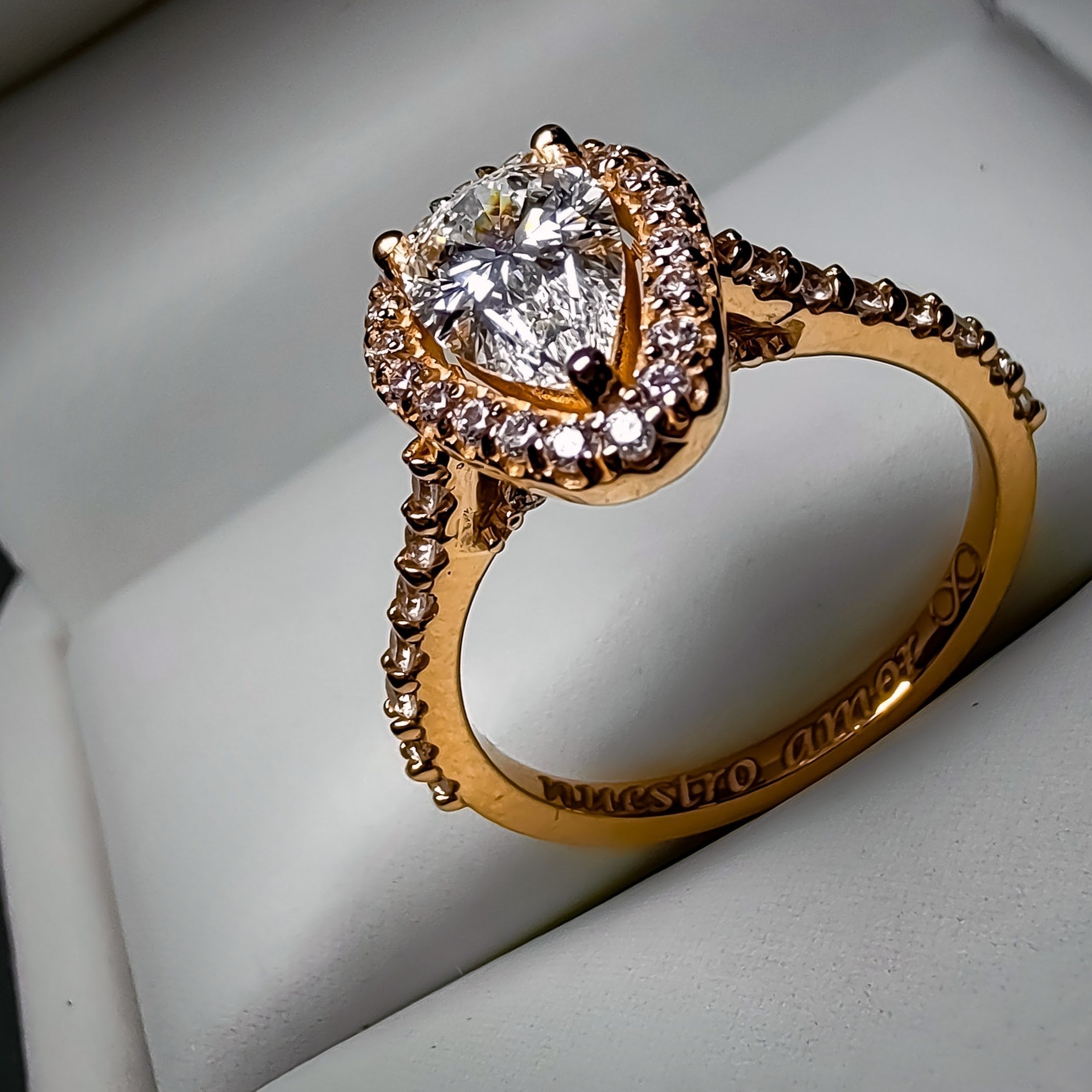 Perfil de anillo de compromiso con diamante en forma de pera, halo y banda pavé en oro rosa, con grabado interior visible