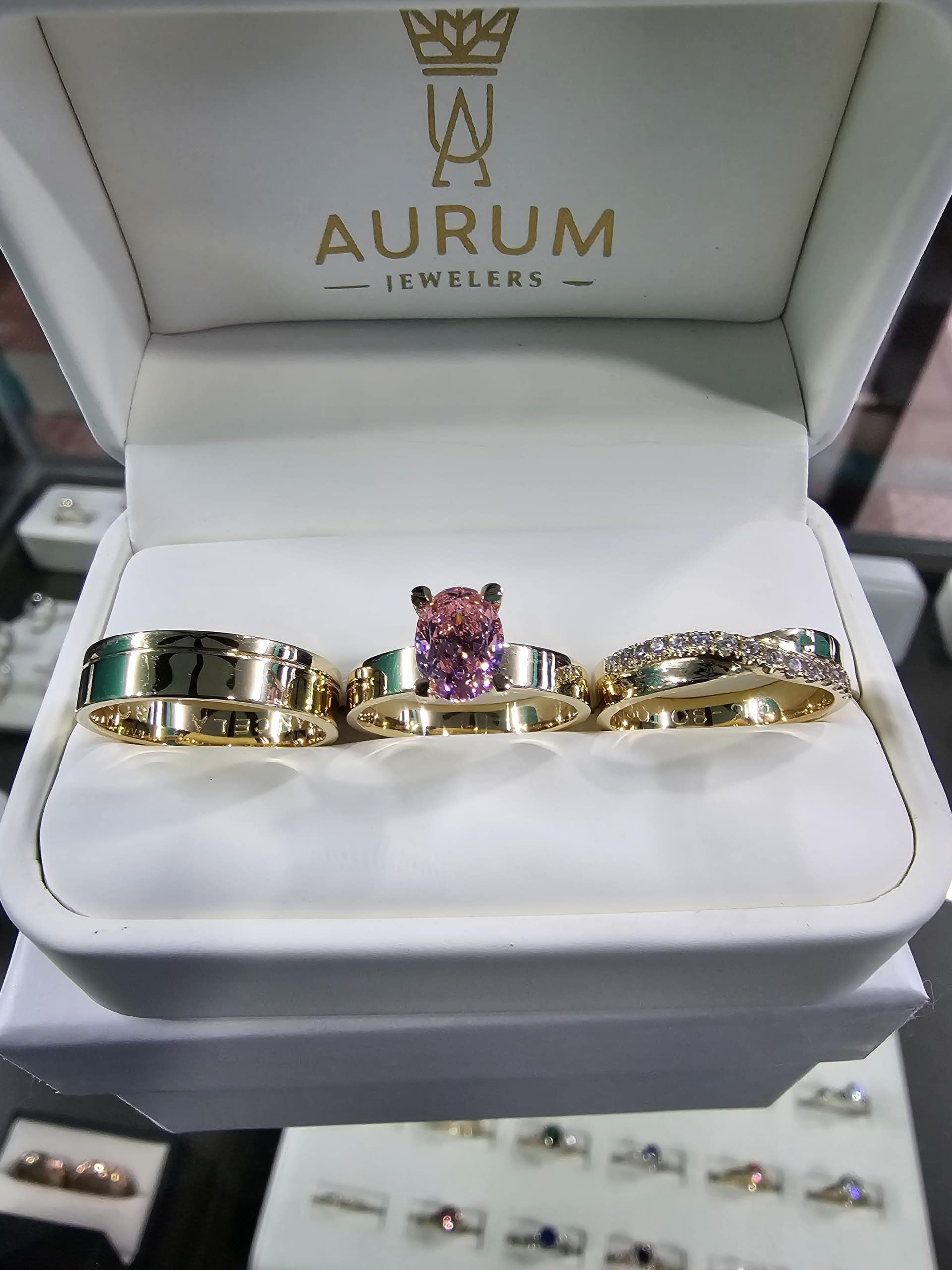 Estuche de trío de anillos sostenido frente a la vitrina del showroom de Aurum