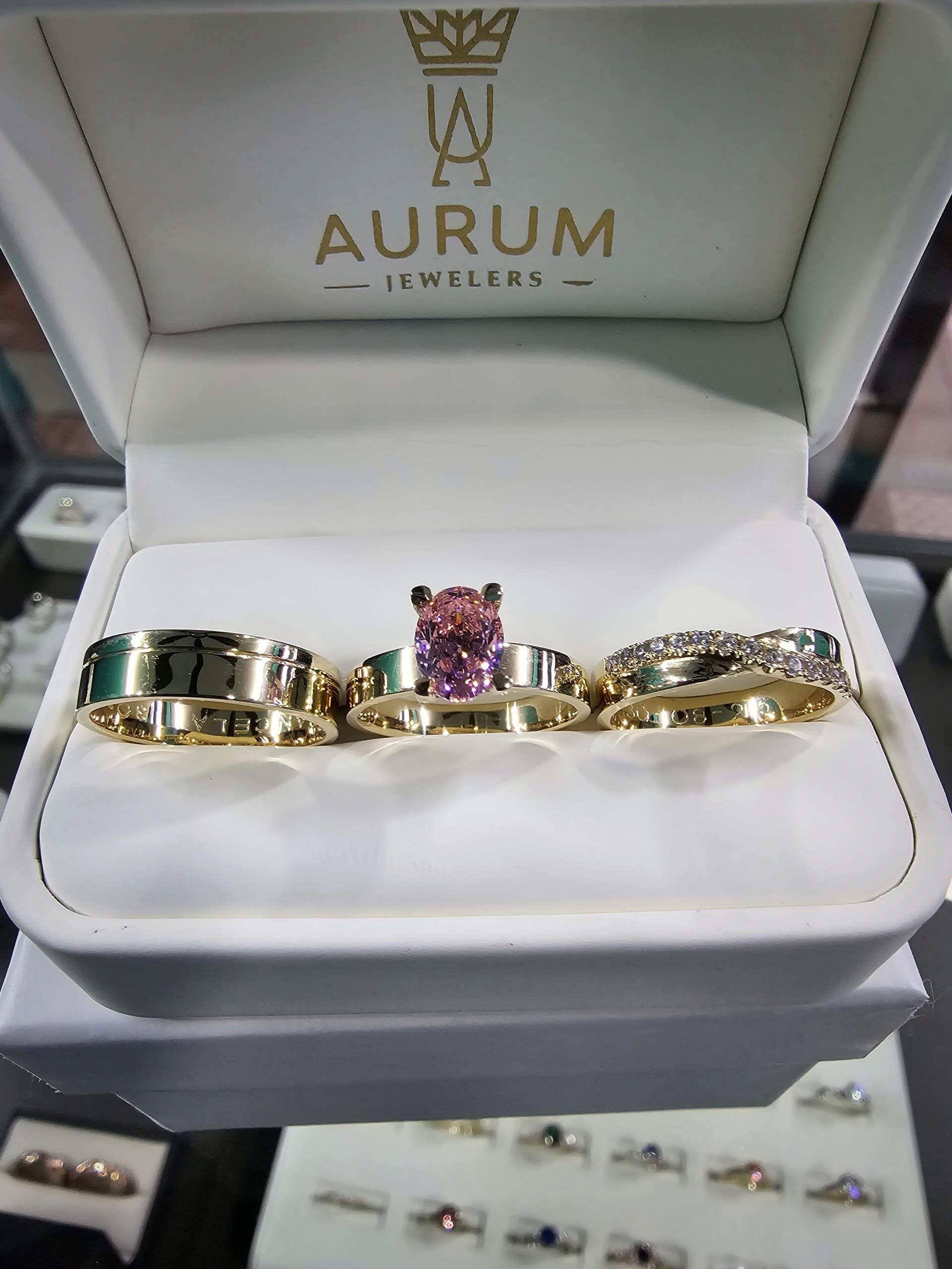 Estuche de trío de anillos sostenido frente a la vitrina del showroom de Aurum
